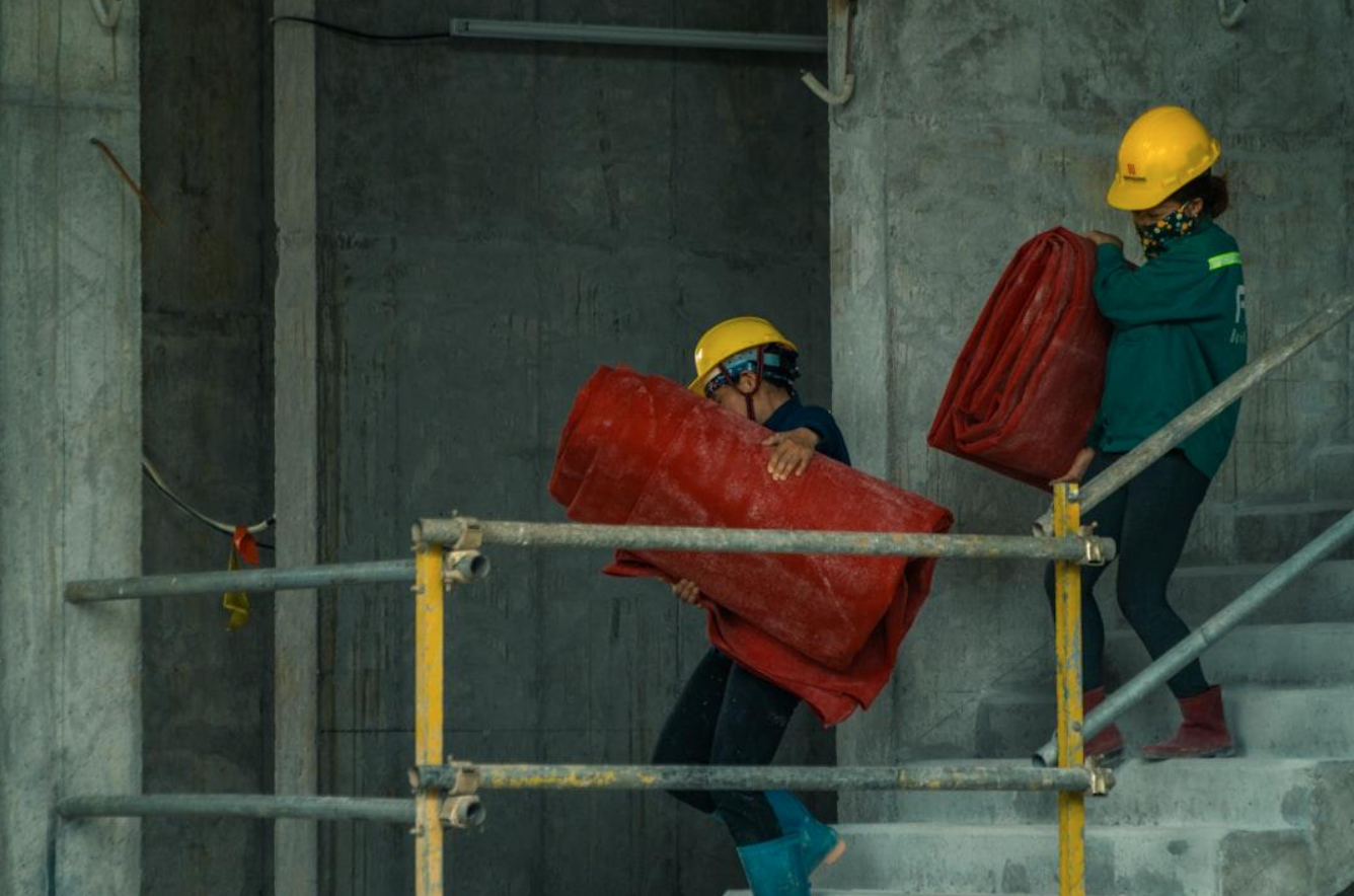 Two men in hardhats carrying red tarps; image by Hoang Kim Hung, via Unsplash.com.